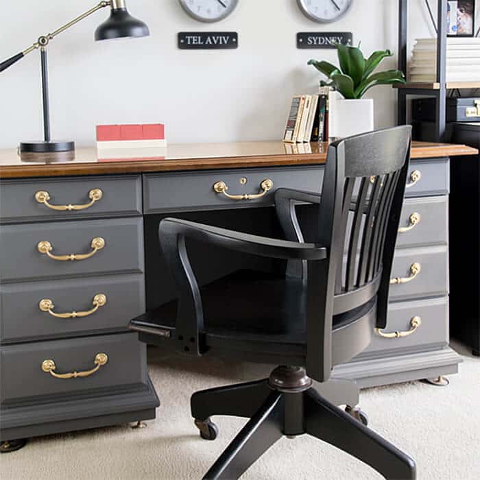 A wooden desk with grey drawers and gold handles. 