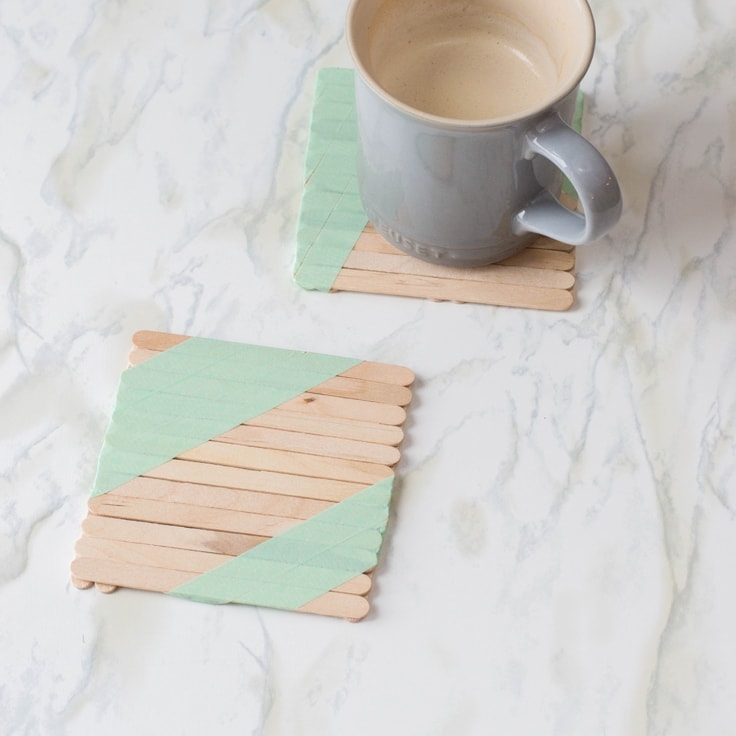 DIY drink coasters made out of popsicle sticks. A grey coffee mug sits on one of them. 