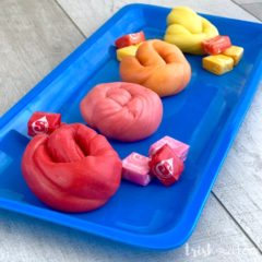 Red, pink, orange and yellow Starburst slime sitting on a bright blue tray with candy pieces.