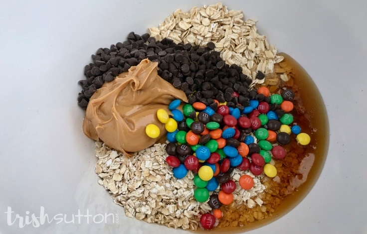 Bowl filled with oats, chocolate chips, M&M candies, peanut butter and honey.