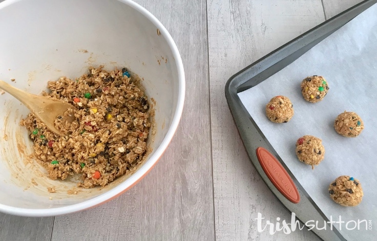 Mixing bowl filled with monster cookie energy bites batter and a plan with dough balls. 