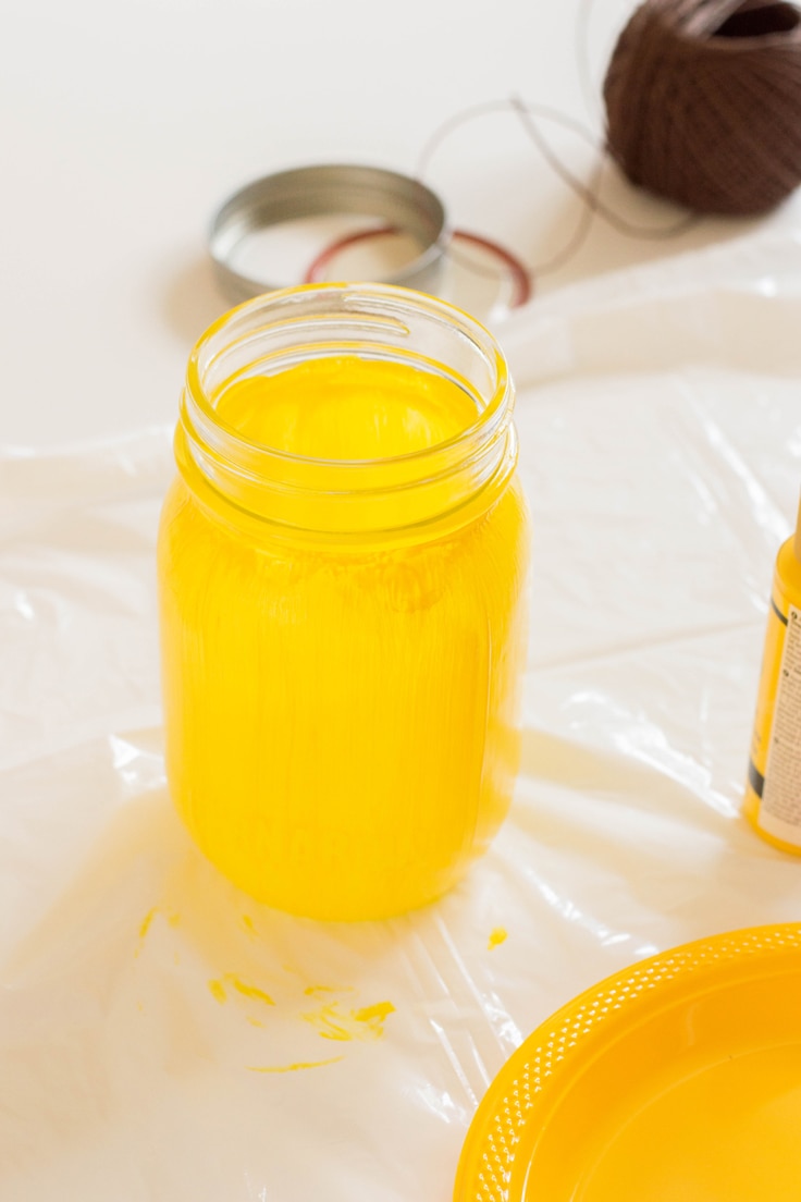 A mason jar with 3 coats of yellow paint on it. 