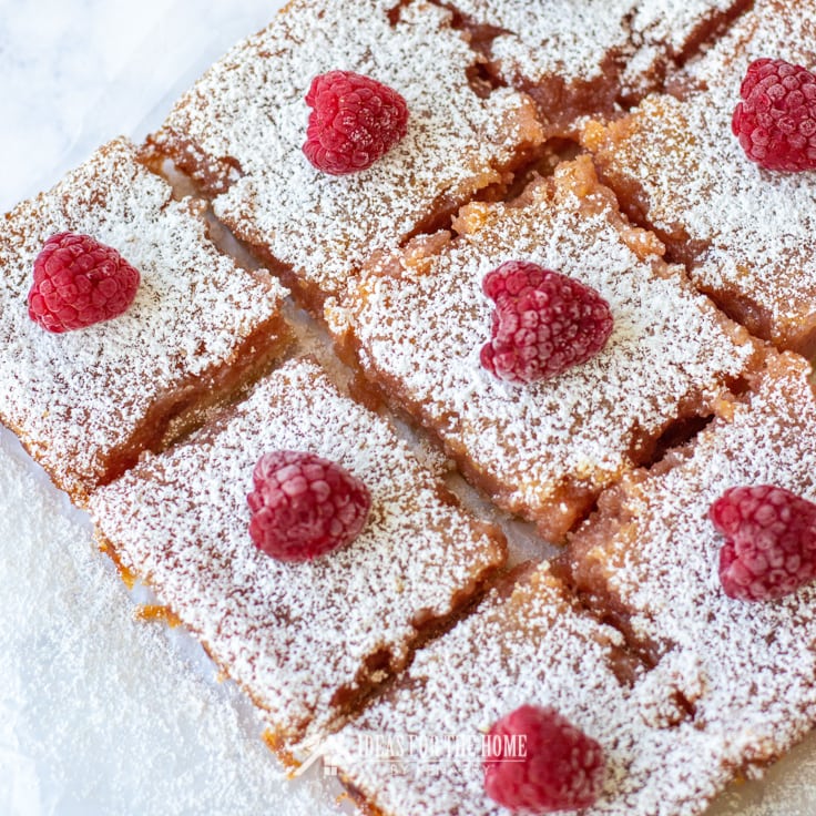 Overhead shot of raspberry lemon bars sprinkled with powdered sugar. Each of these summer desserts is topped with a single plump juicy raspberry.