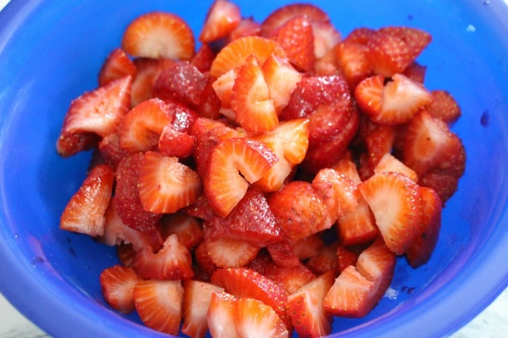 cut up strawberries in blue bowl with sugar