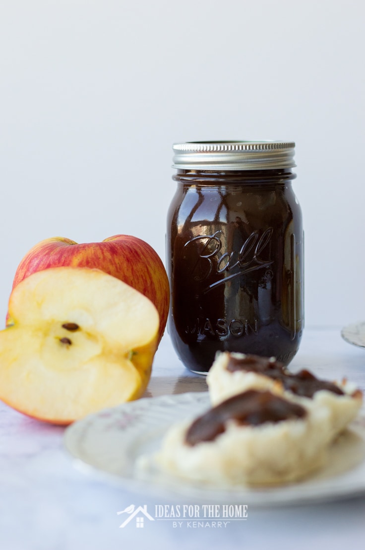 A jar of apple butter, an apple and a biscuit spread with apple butter