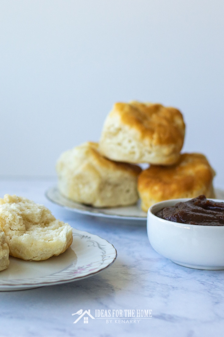 Biscuits fresh from the oven stacked on plates next to a bowl of easy homemade apple butter