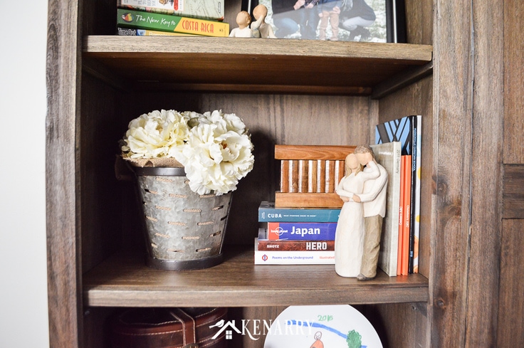 A galvanized metal olive basket filled with burlap and large flowers gives a book shelf farmhouse style
