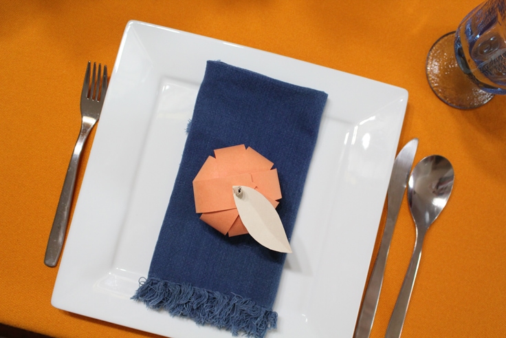aerial view of an orange paper pumpkin with a manila paper leaf and stem at a place setting