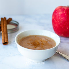 Bowl of applesauce with cinnamon sticks and a fresh apple