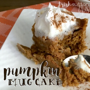 pumpkin mug cake topped with whipped cream and resting on a white plate