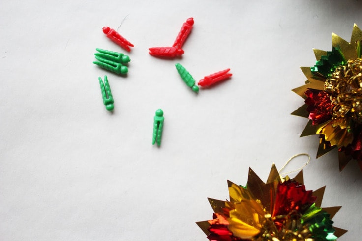 Vintage ornaments made out of foil laying next to red and green plastic clothes pins. 