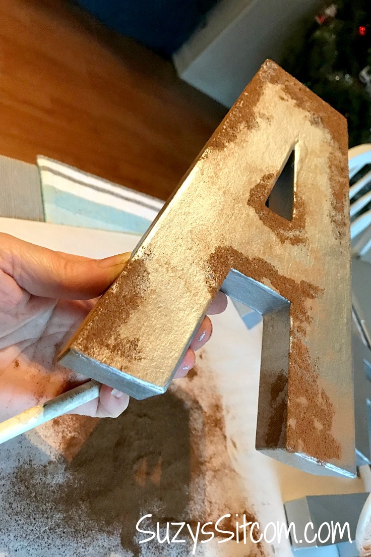 A large letter A painted silver with cinnamon sprinkled on it to look like rust. 