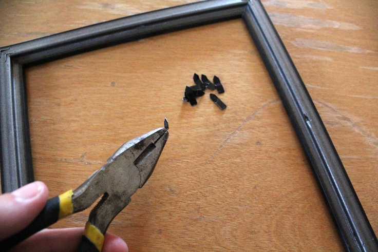 Plier holding a metal pin. A frame and several metal pins sit in the background.
