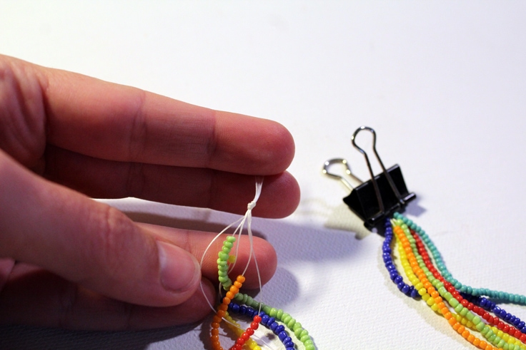 hand tying a knot at the end of the gathered strands of beads