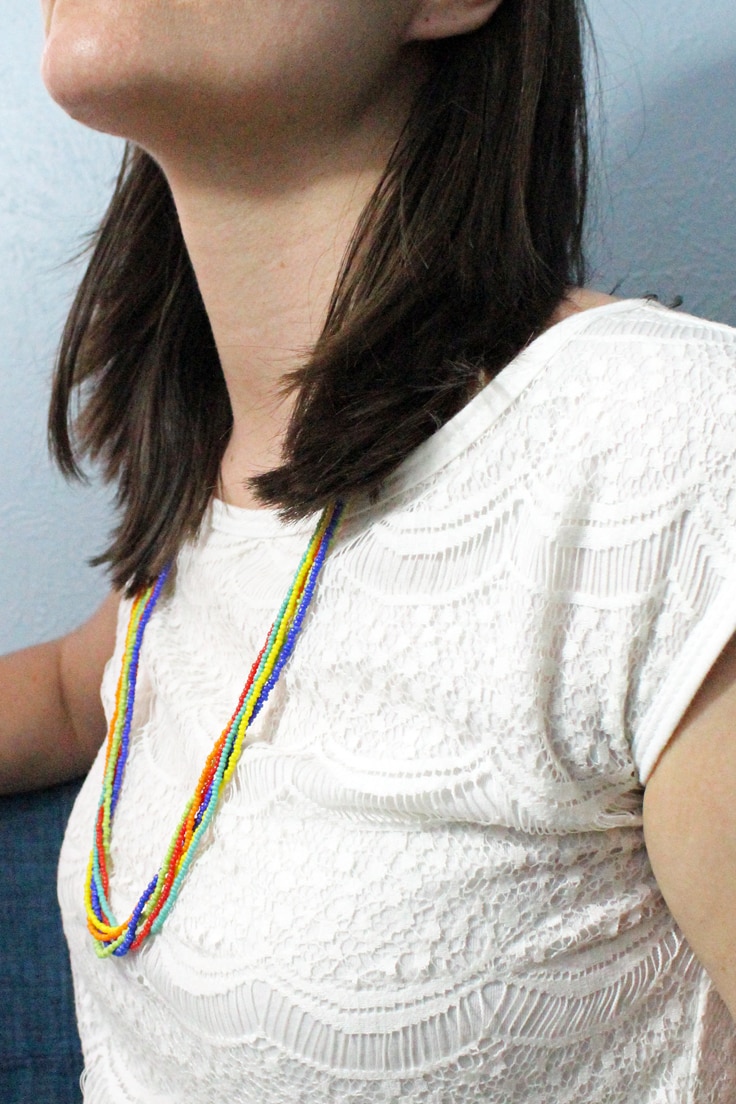 woman in a white dress wearing a beaded necklace with each strand a single color of the rainbow