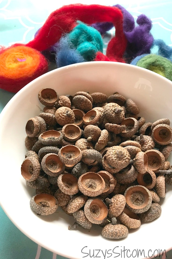 A bowl of acorn caps and lots of colorful wool yarn next to it. 