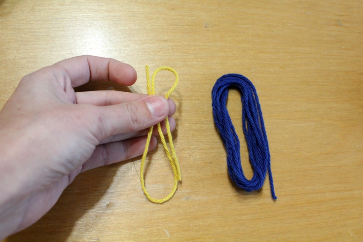 hand holding a short piece of yellow yarn beside a bundle of blue yarn