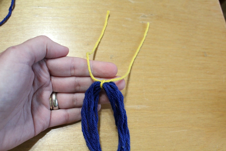 hand tying yellow yarn around blue yarn