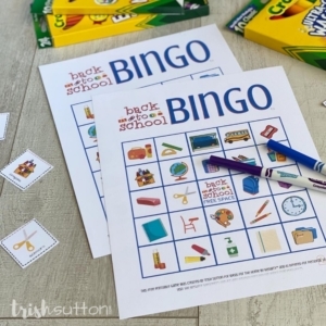 Two Bingo cards on a wood background surrounded by game pieces and markers.