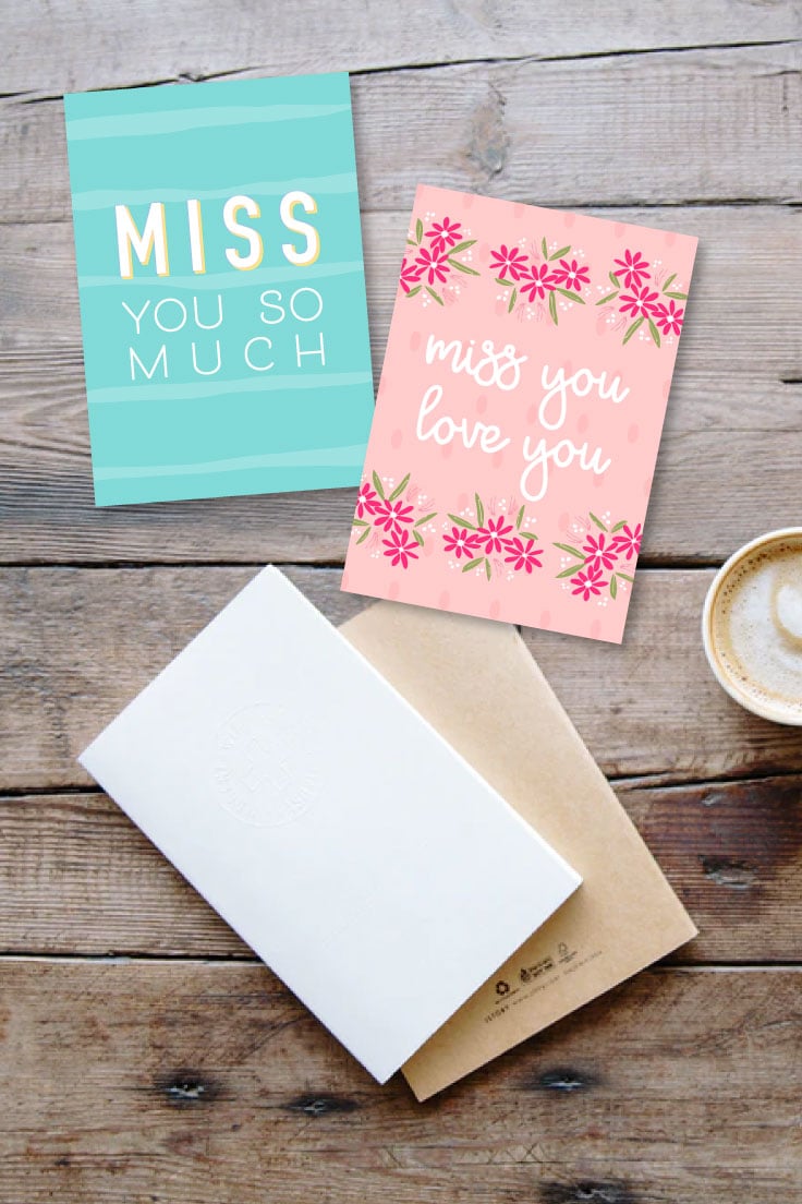 Miss you so much and miss you love you card designs on wooden tabletop with envelopes and a mug of coffee.