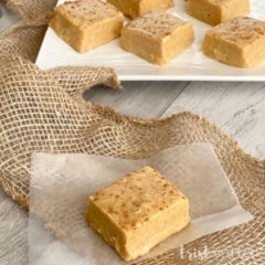A piece of pumpkin fudge resting on burlap with a plate of fudge in the background.
