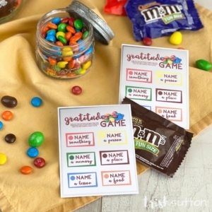 Gratitude game cards with M&Ms on a yellow fabric background.