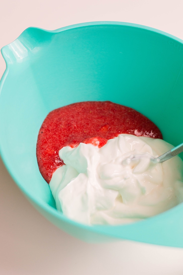 Greek yogurt and strawberry puree being mixed in a bowl to create easy frozen yogurt bites.
