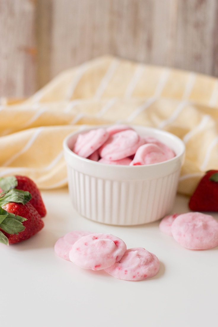 A bowl of Easy Strawberry Yogurt Bites with some scattered by it, with fresh strawberries to accompany.