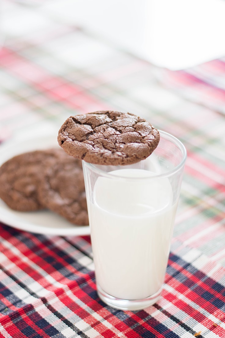 A chocolate cookie sitting on a tall glass of milk.