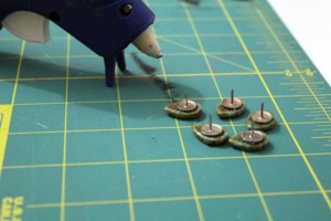 leaf beads being glued to the head of several thumbtacks with hot glue