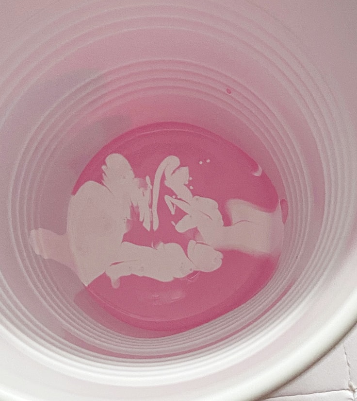 White paint poured into pink paint in a plastic cup.