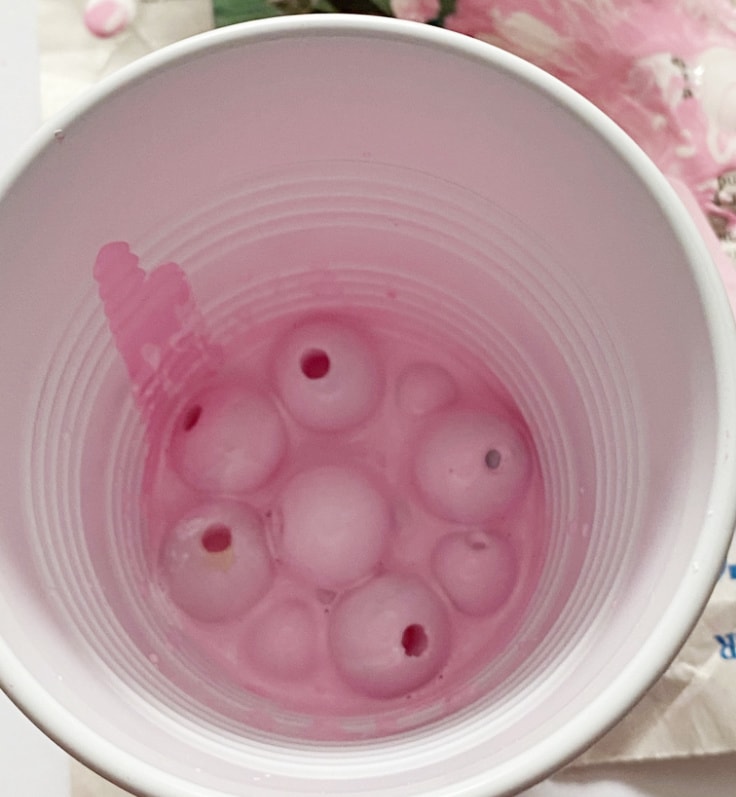 Wood beads in a cup of pink of paint.