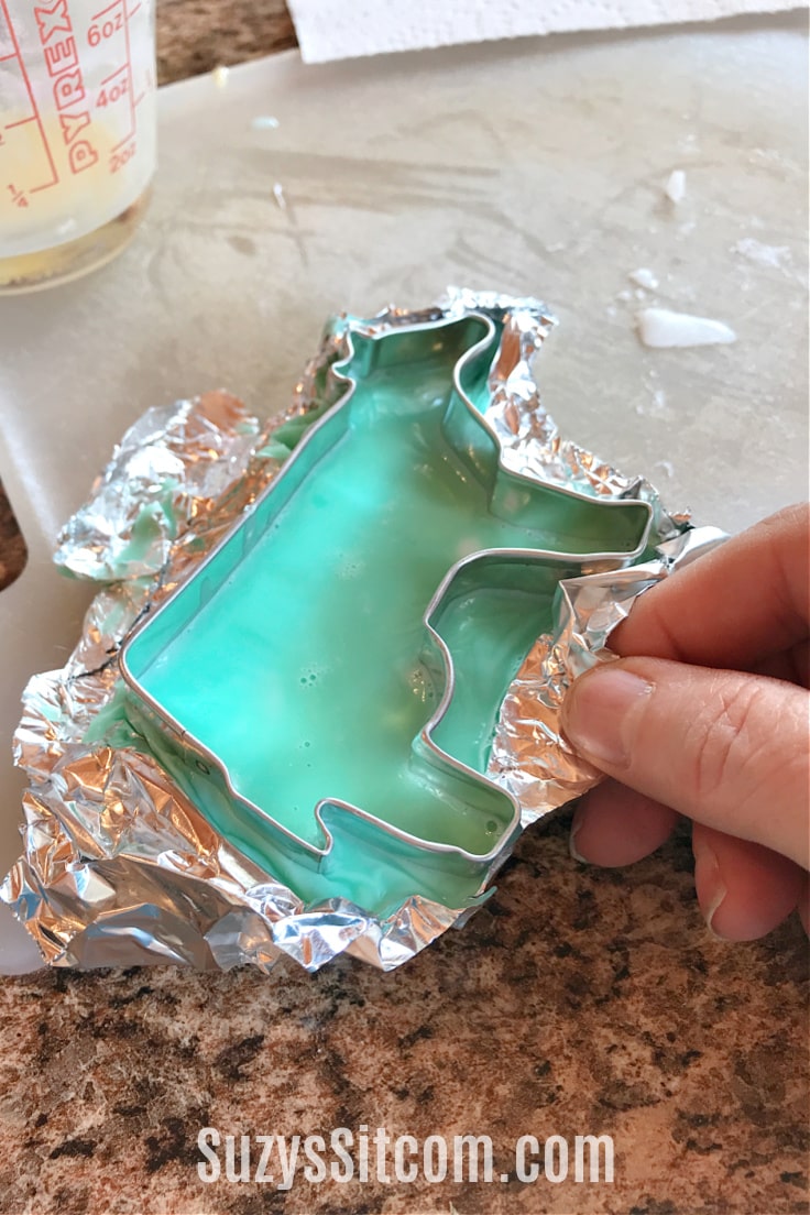 A blue melt and pour soap inside a metal cookie cutter shaped like a cow.