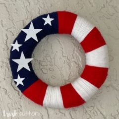 Wreath covered in stars and stripes hanging on white stucco.