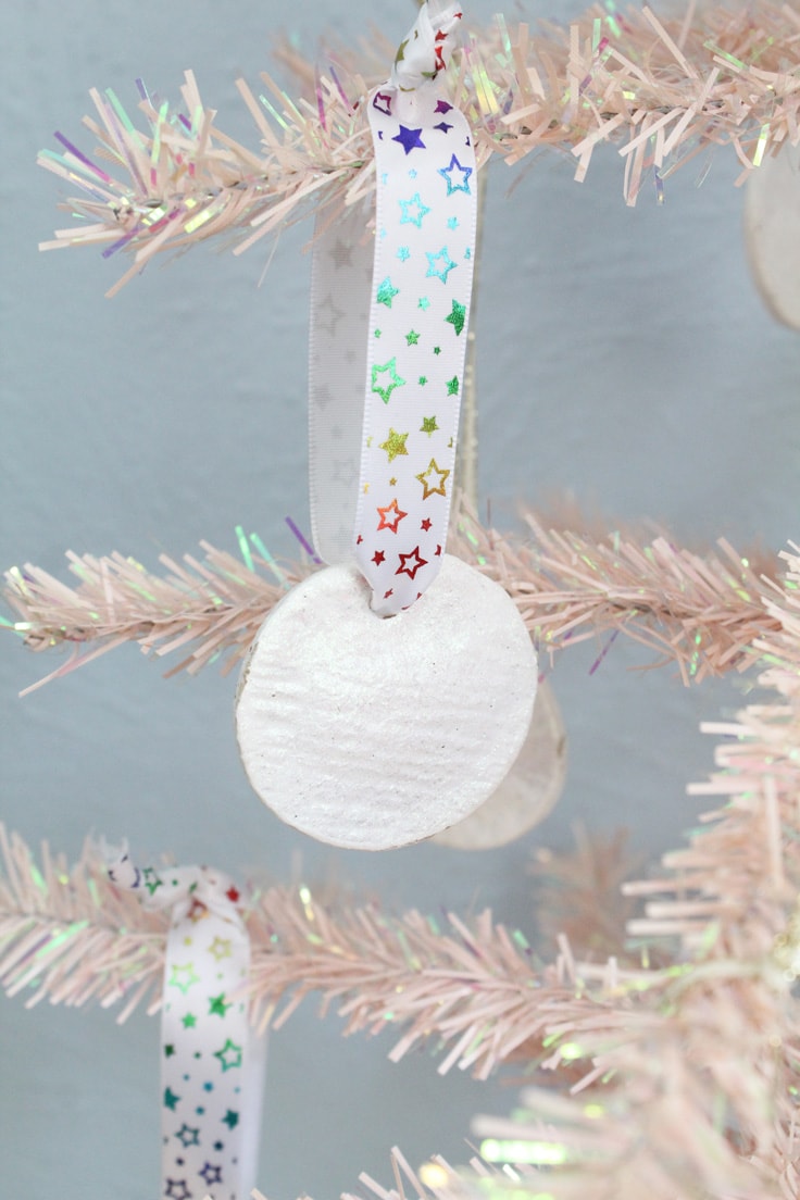 White glittery salt dough Christmas ornament hanging on a rainbow star patterned ribbon.