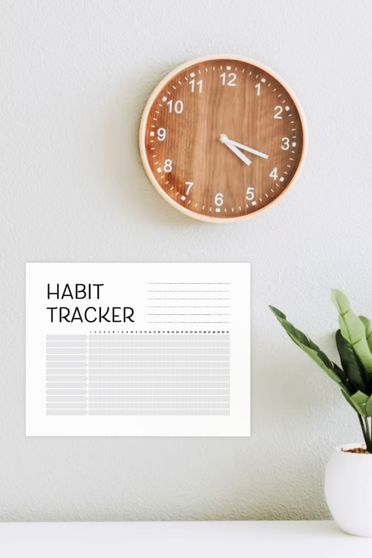 Preview of PDF of habit tracker taped to white wall with wooden analog clock and potted plant on the right. 