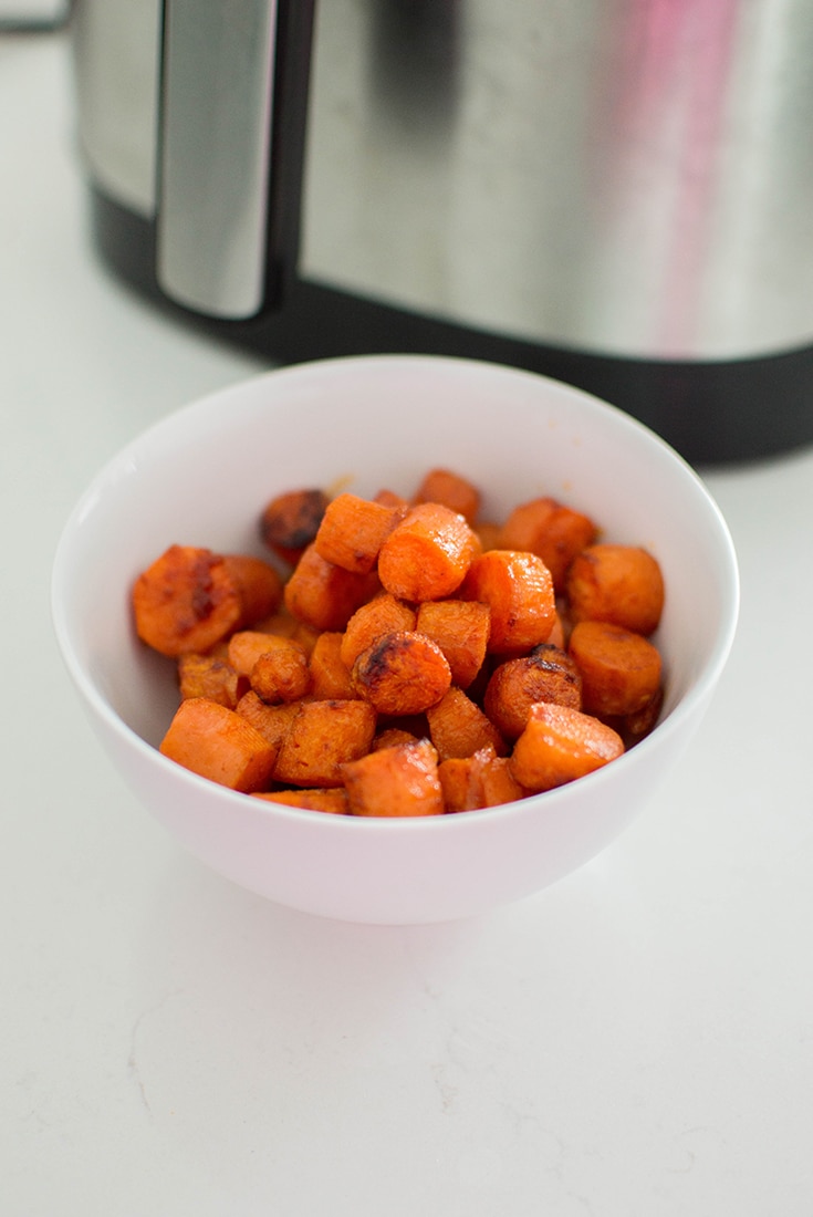 Bowl of honey glazed carrots in front of an air fryer.
