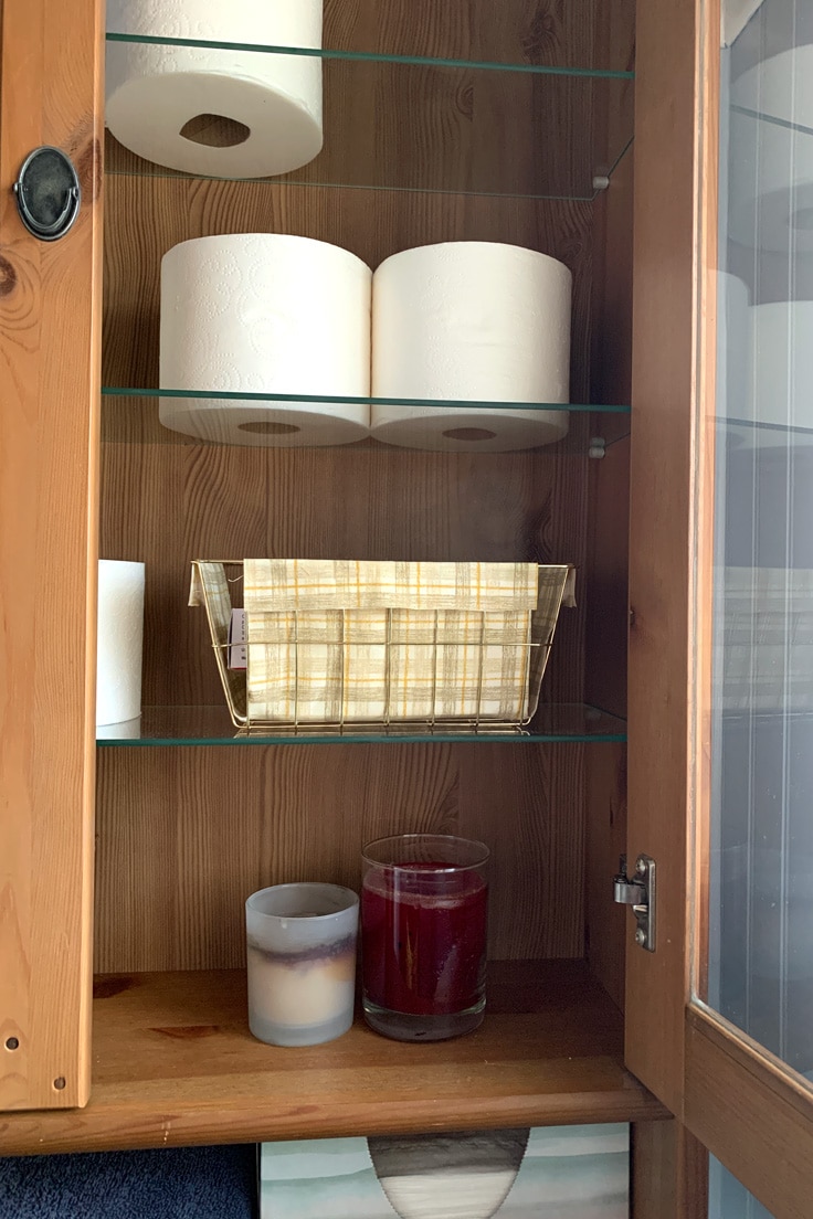 Bathroom cabinet with fabric lined storage baskets and toilet paper rolls on a shelf.