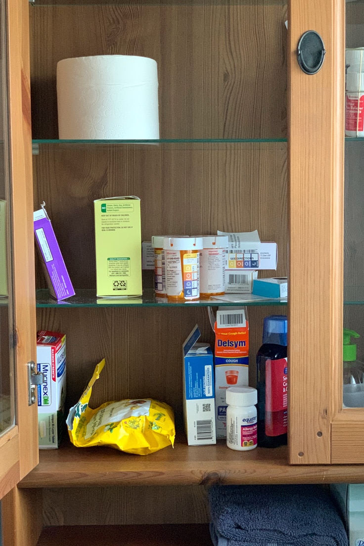 Messy bathroom medicine cabinet with bottles and boxes of products scattered on shelves.