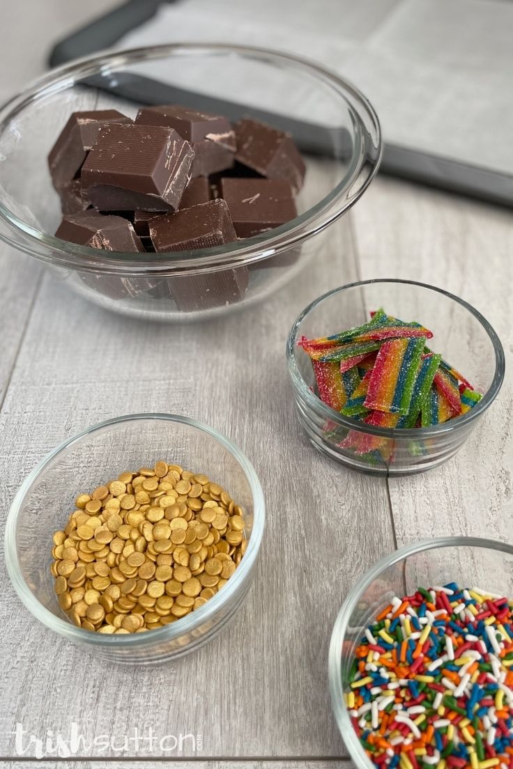 Four ingredients for Rainbow Chocolate Bark on a wood background with a prepared pan.