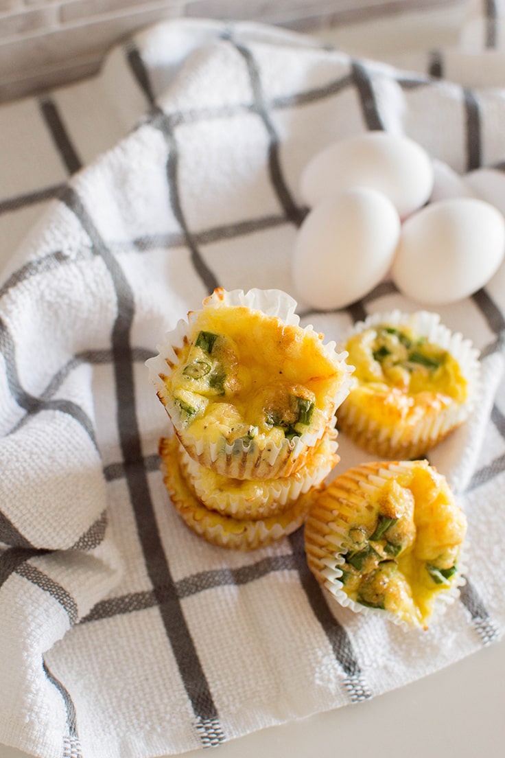 Green onion and cheese egg muffins stacked on a grey and white napkin