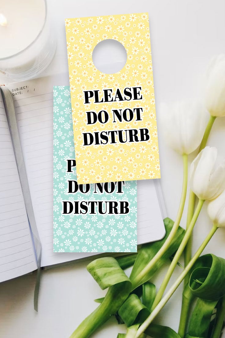 Preview of printable door hanger designs on white desk with white candle, lined notebook and white tulip flowers. 