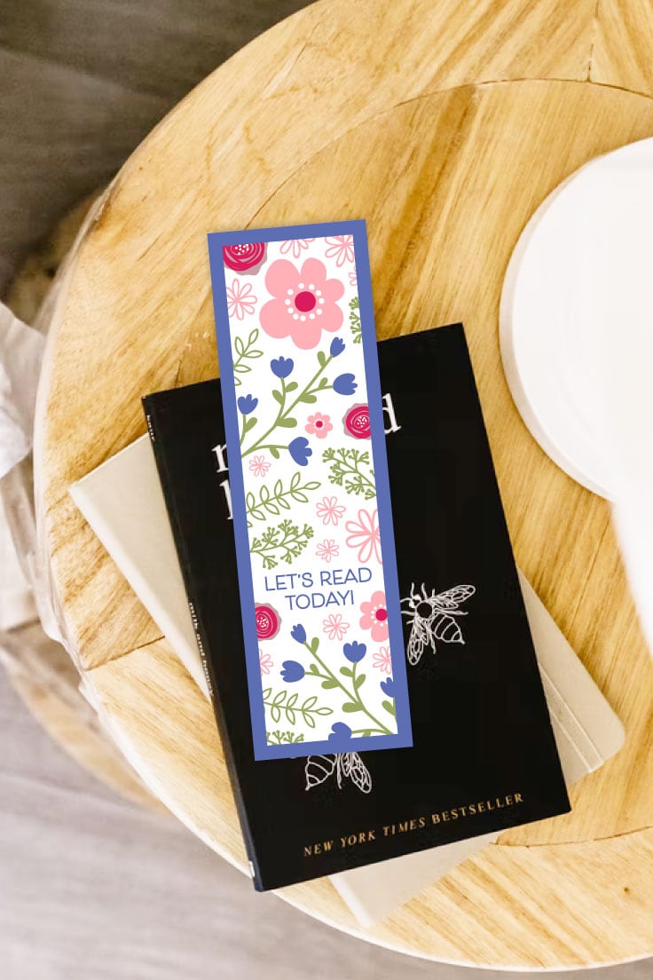 Preview of purple and pink floral printable bookmark on top of books resting on top of wooden bedside table.