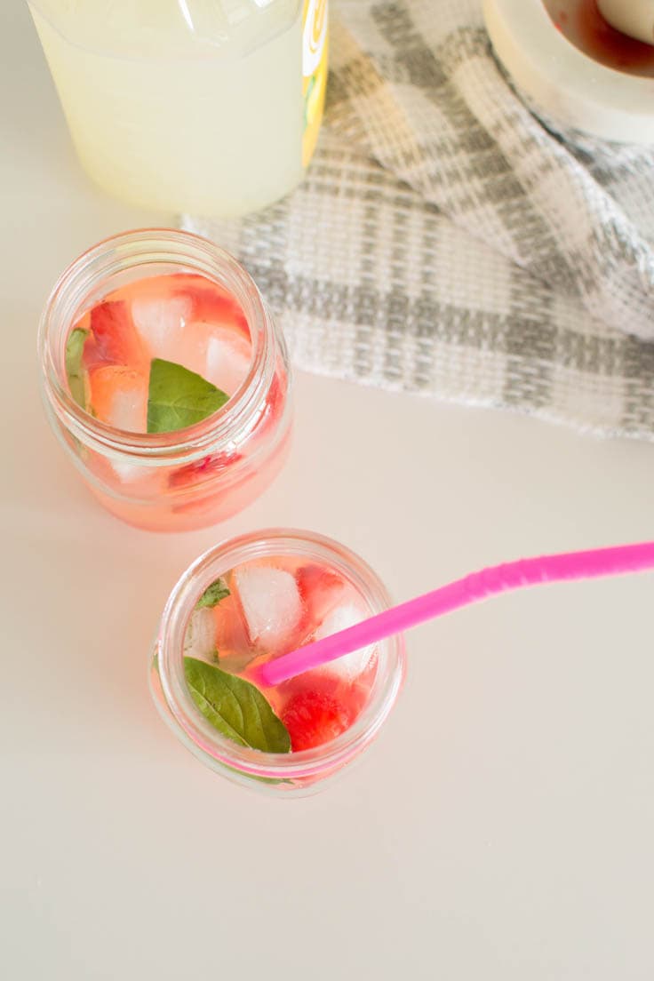 Bird's eye view of strawberry basil lemonade in mason jars. One serving has a bright pink straw.