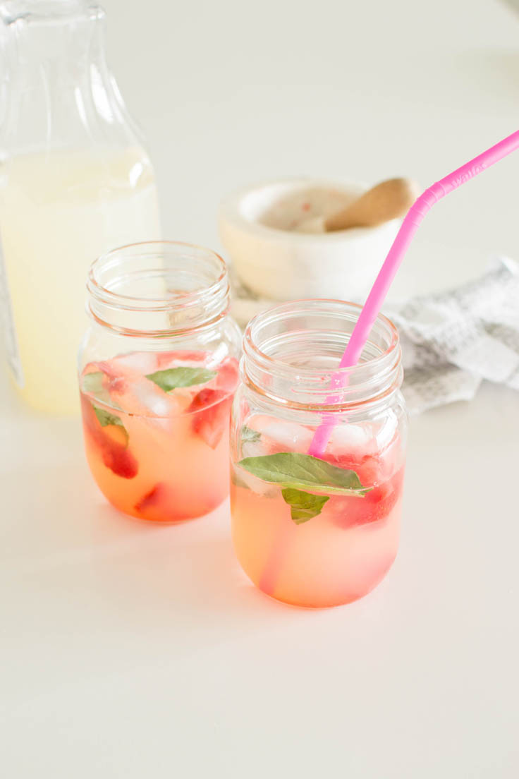 Two mason jars filled with lemonade, infused with strawberry and basil. One mason jar has a hot pink straw.