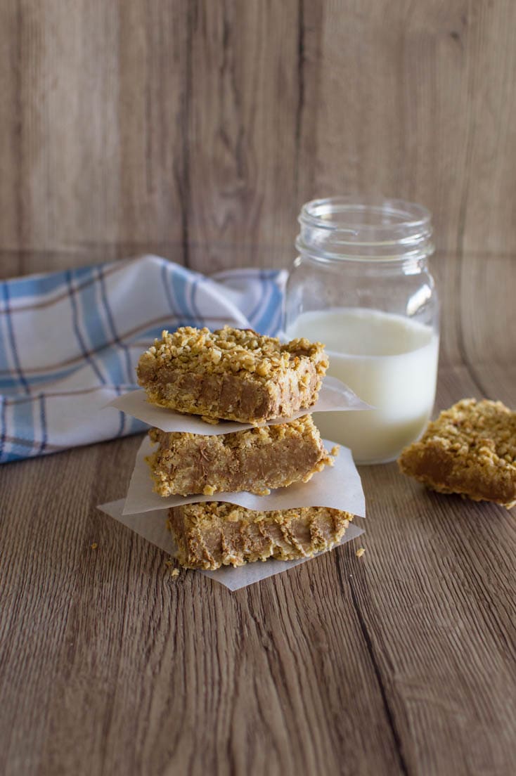 A stack of no-bake chocolate oatmeal bars with parchment paper in between, sitting on a wooden table, with a mason jar of milk in the background