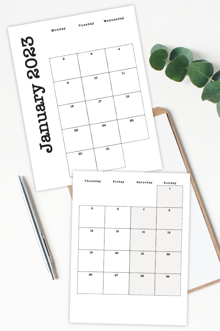 Preview of January 2023 monthly printable calendar pages on white desk with silver pen and notebooks underneath and green leaves in upper right hand corner.