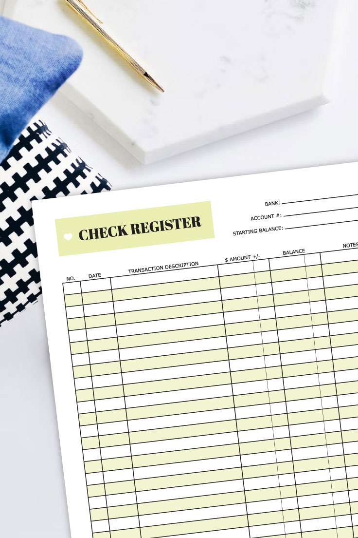 Preview of check register PDF on top of white desk with pillows, gold pen and white marble desk accessory in the background.