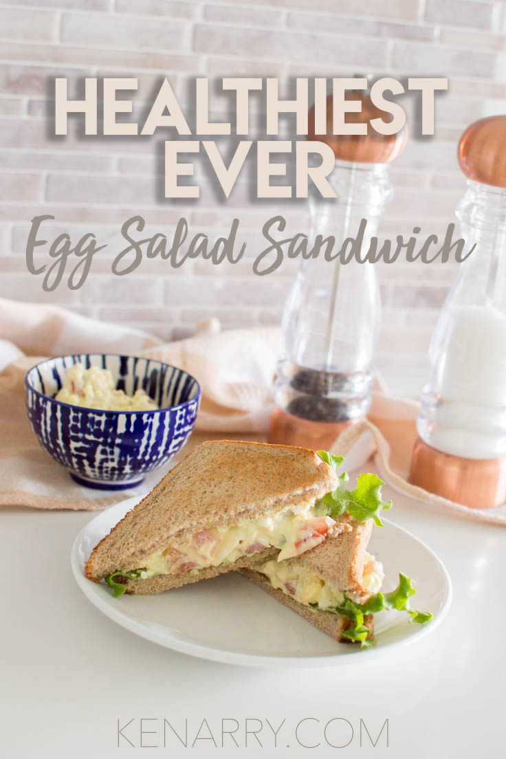 An egg salad sandwich cut into triangle halves, sitting on a white plate with salt and pepper shakers and a blue bowl in the background