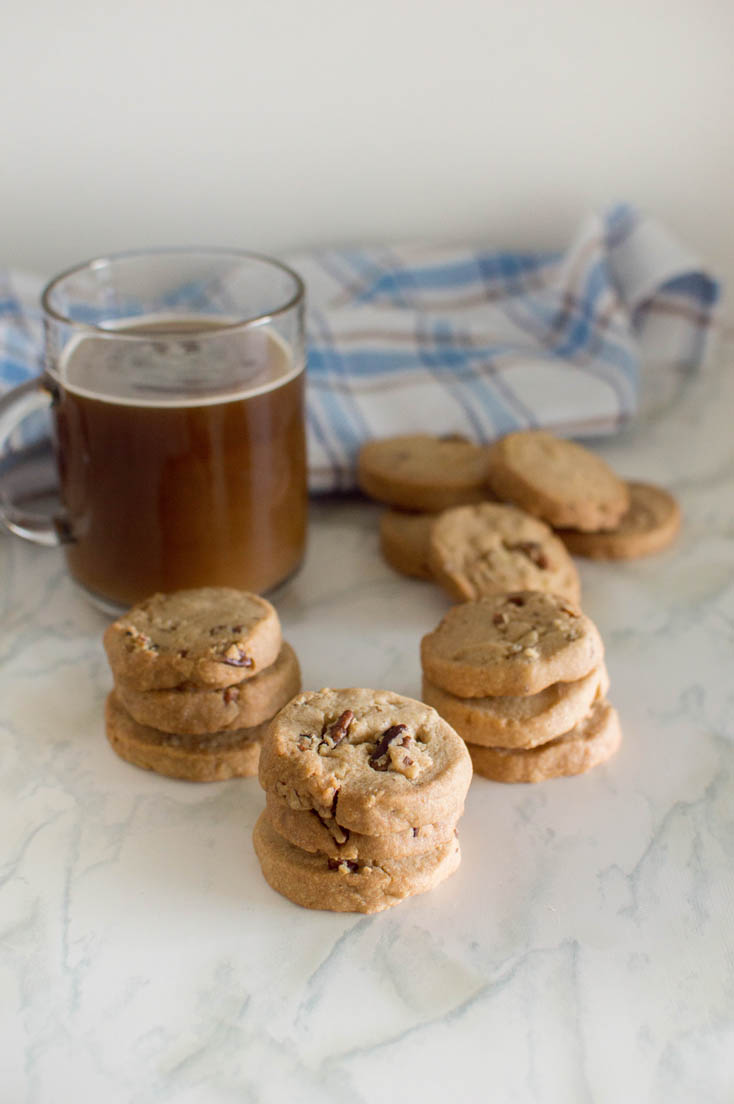 Three stacks of homemade pecan shortbread cookies with a glass mug of coffee in the background and a blue plaid napkin